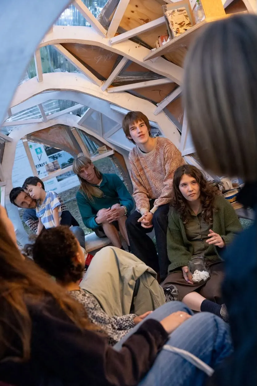 Des jeunes discutent ensemble dans une construction en bois en forme de dôme aux parois vitrées.