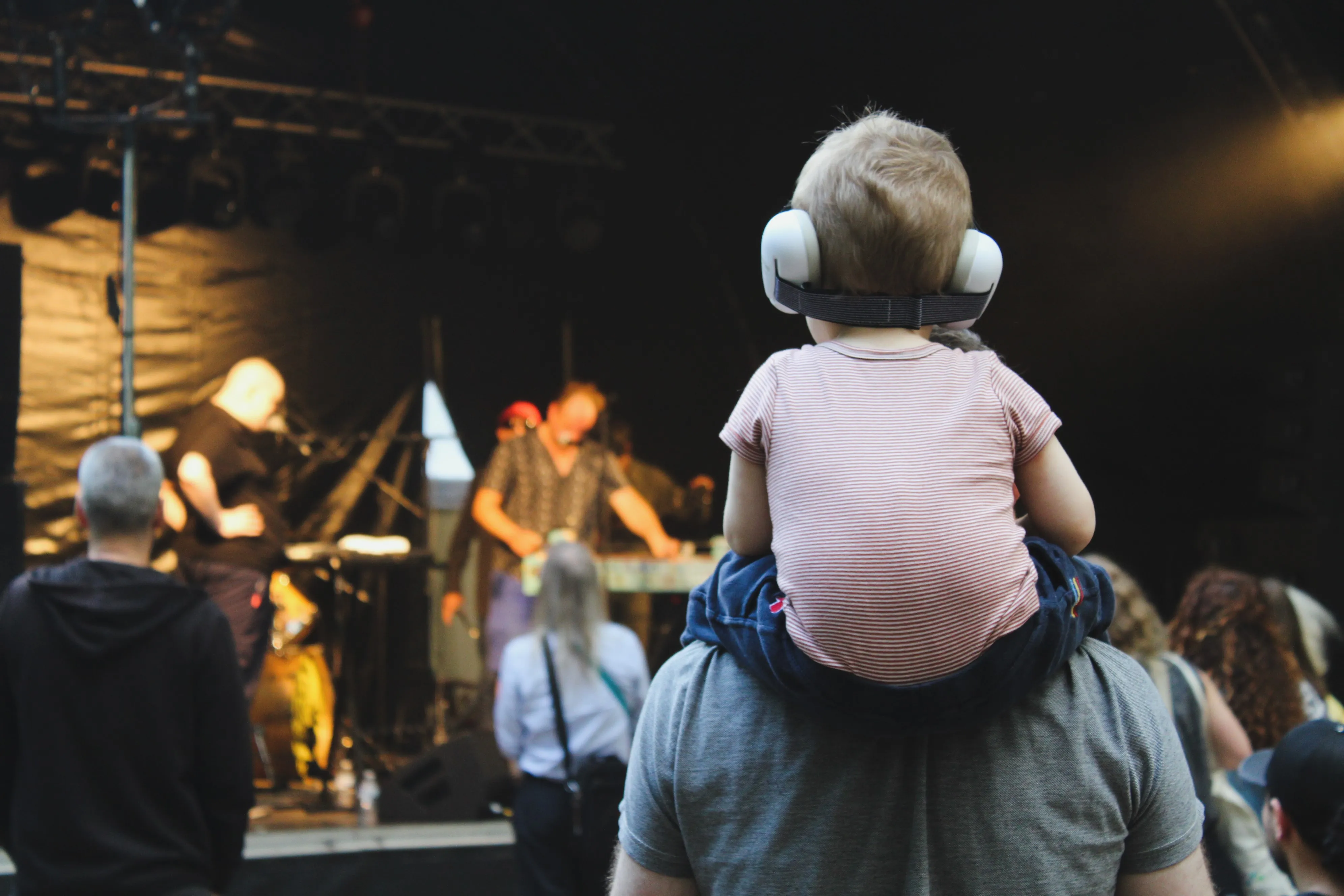 Un enfant avec une protection auditive sur les épaules d'un parent, regardant un spectacle.