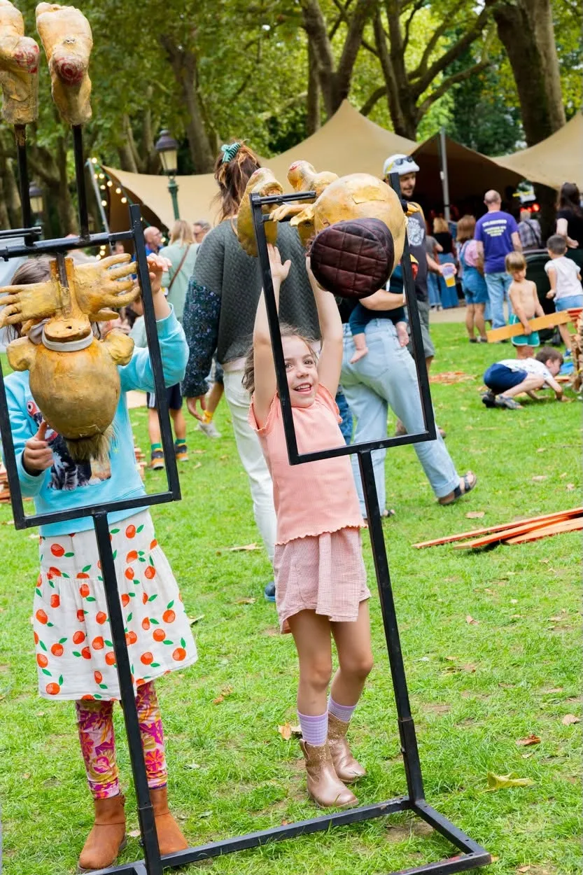 Deux filles soulèvent des têtes de marionnettes dorées sur des cadres noirs, en riant dans le parc.