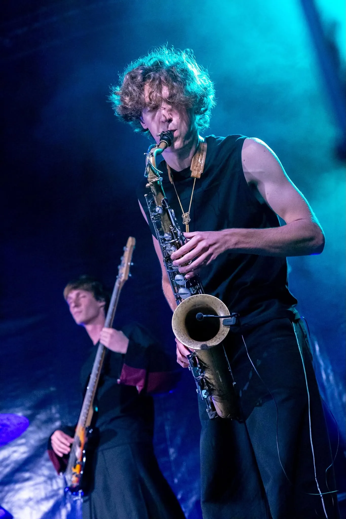 Un saxophoniste joue dans une lumière bleue, un bassiste derrière lui.