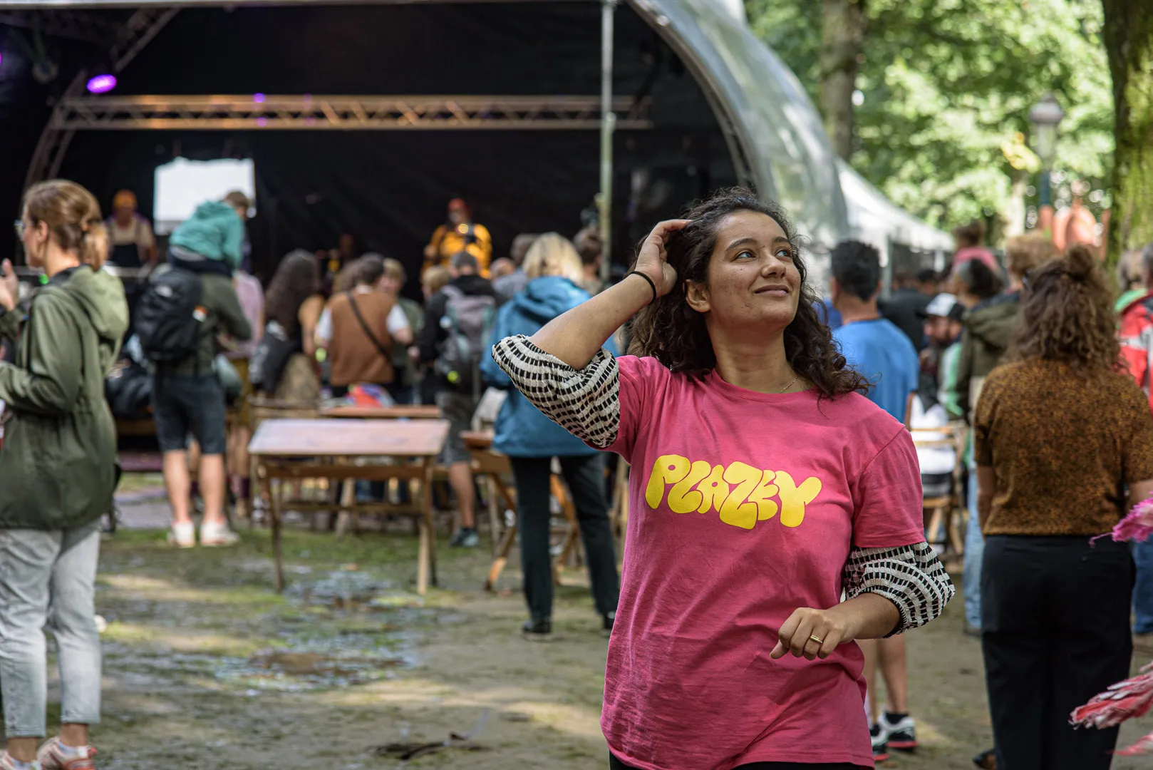 Une bénévole en t-shirt rose Plazey regarde vers le haut, avec le site du festival derrière elle.